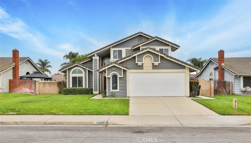 Two-story gray house with white trim, a white garage door, and a green lawn under a blue sky.
