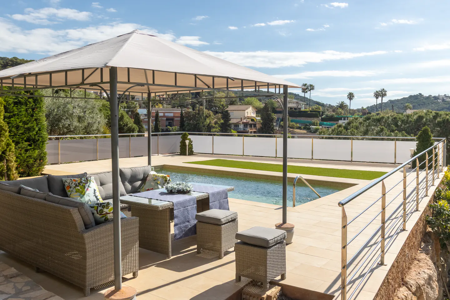 Outdoor patio with wicker furniture, a gazebo, and a pool. Green hills and a blue sky are in the background.