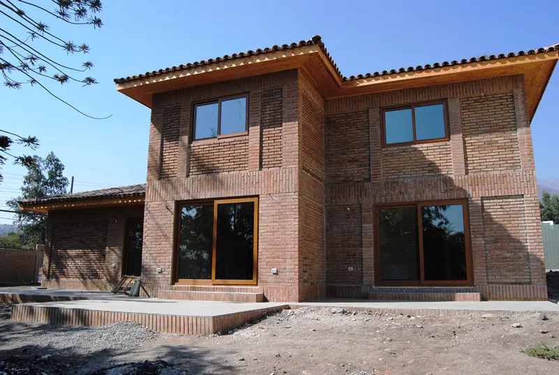 Two-story brick house with wood trim and brown-framed windows under a clear blue sky.