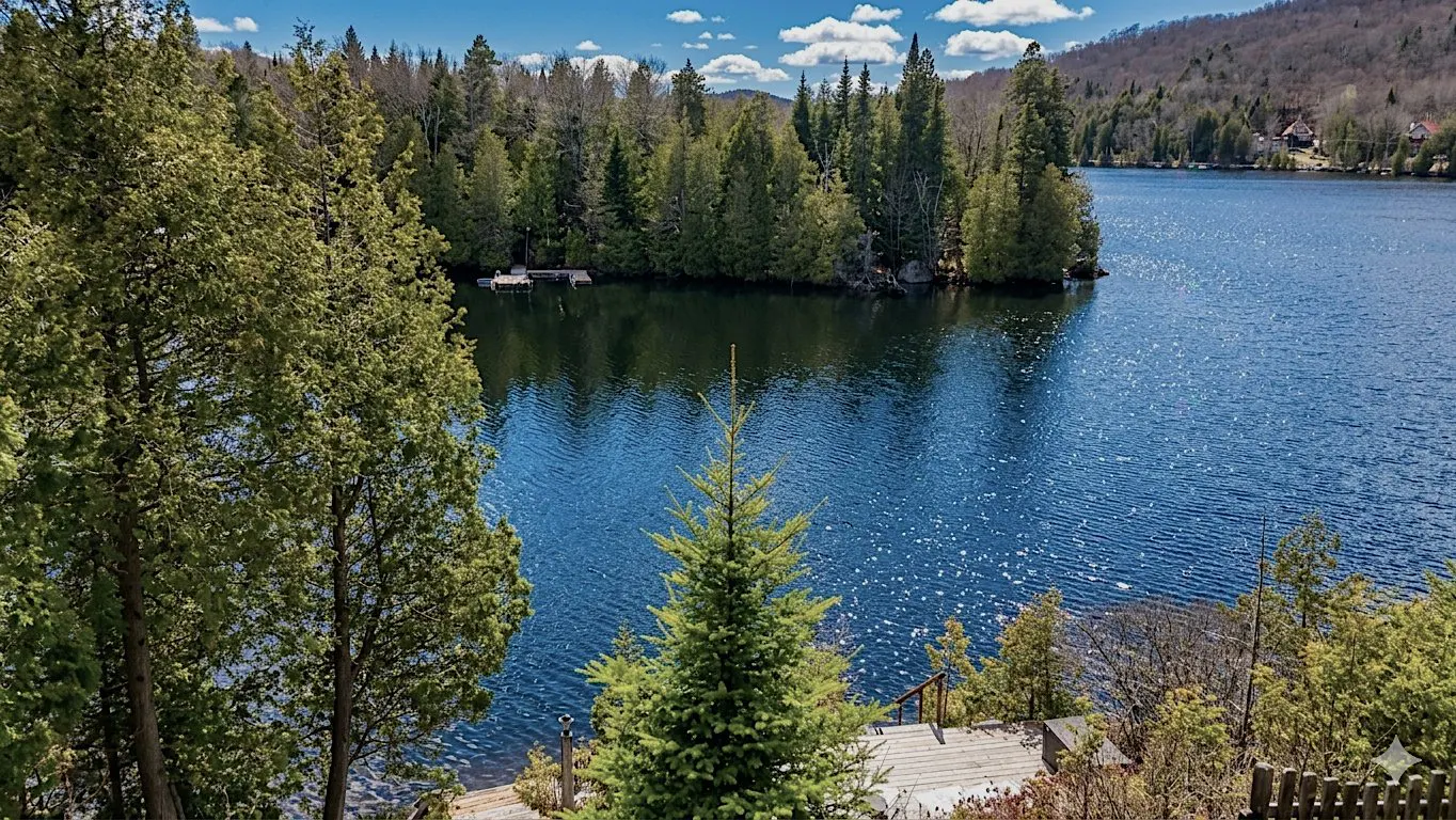 Scenic view of a blue lake surrounded by green trees and a dock, under a partly cloudy sky.
