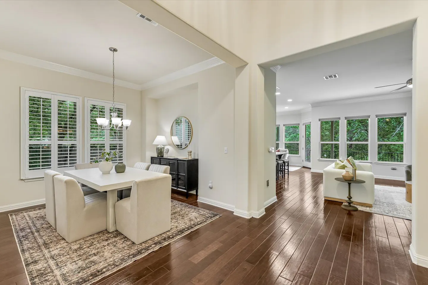 Bright, open-concept home with dining area featuring a white table, chairs, and a chandelier, flowing into a living room with large windows.