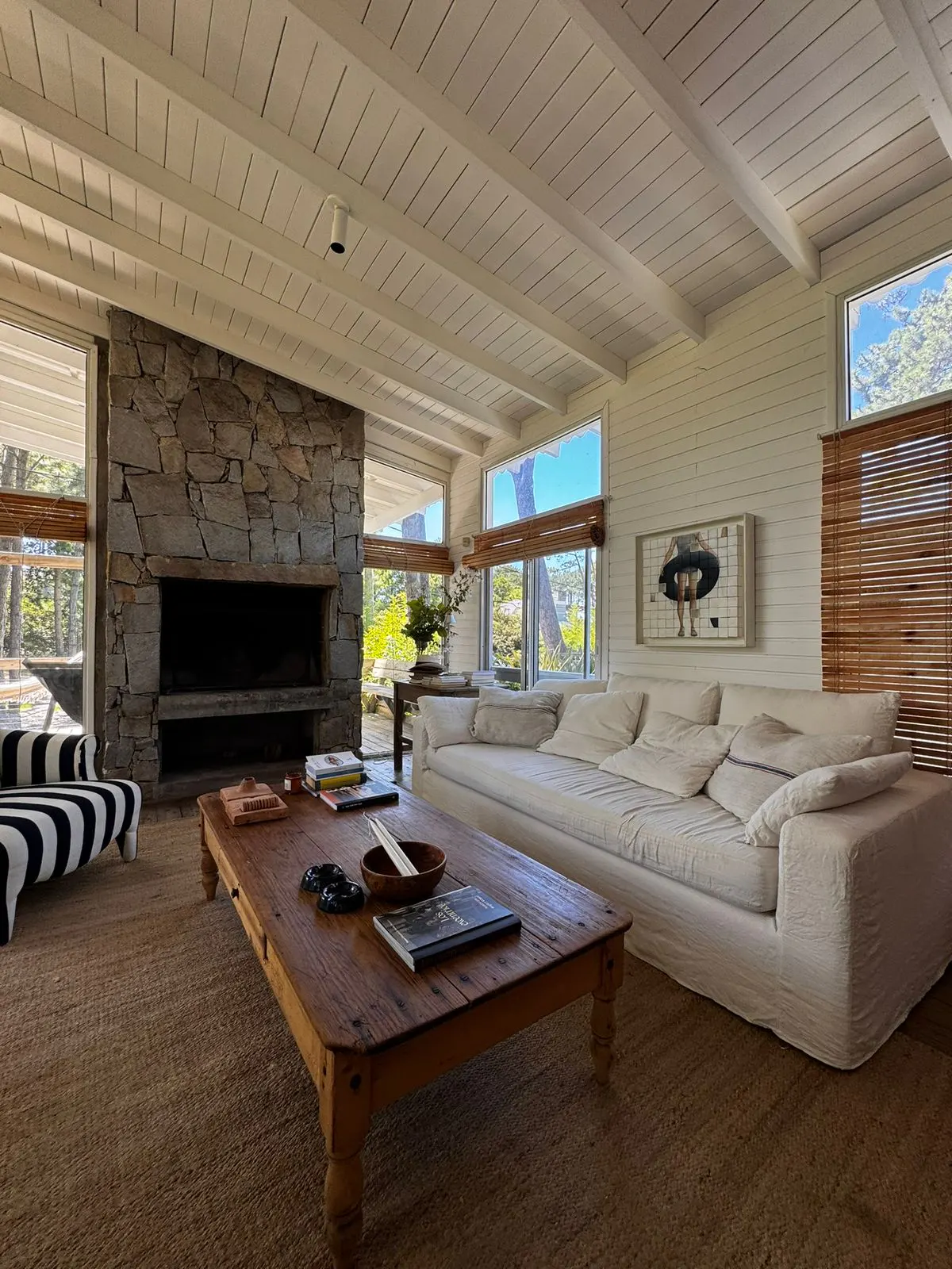 Bright living room with stone fireplace, white sofa, and wood coffee table on a jute rug. Windows with bamboo blinds let in natural light.