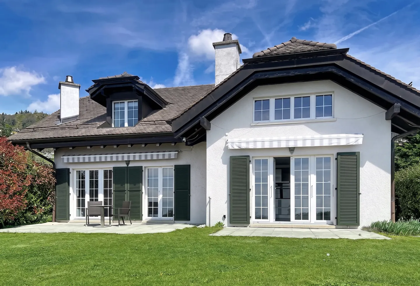 Exterior of a two-story white house with dark green shutters and a brown roof. A green lawn is in front.