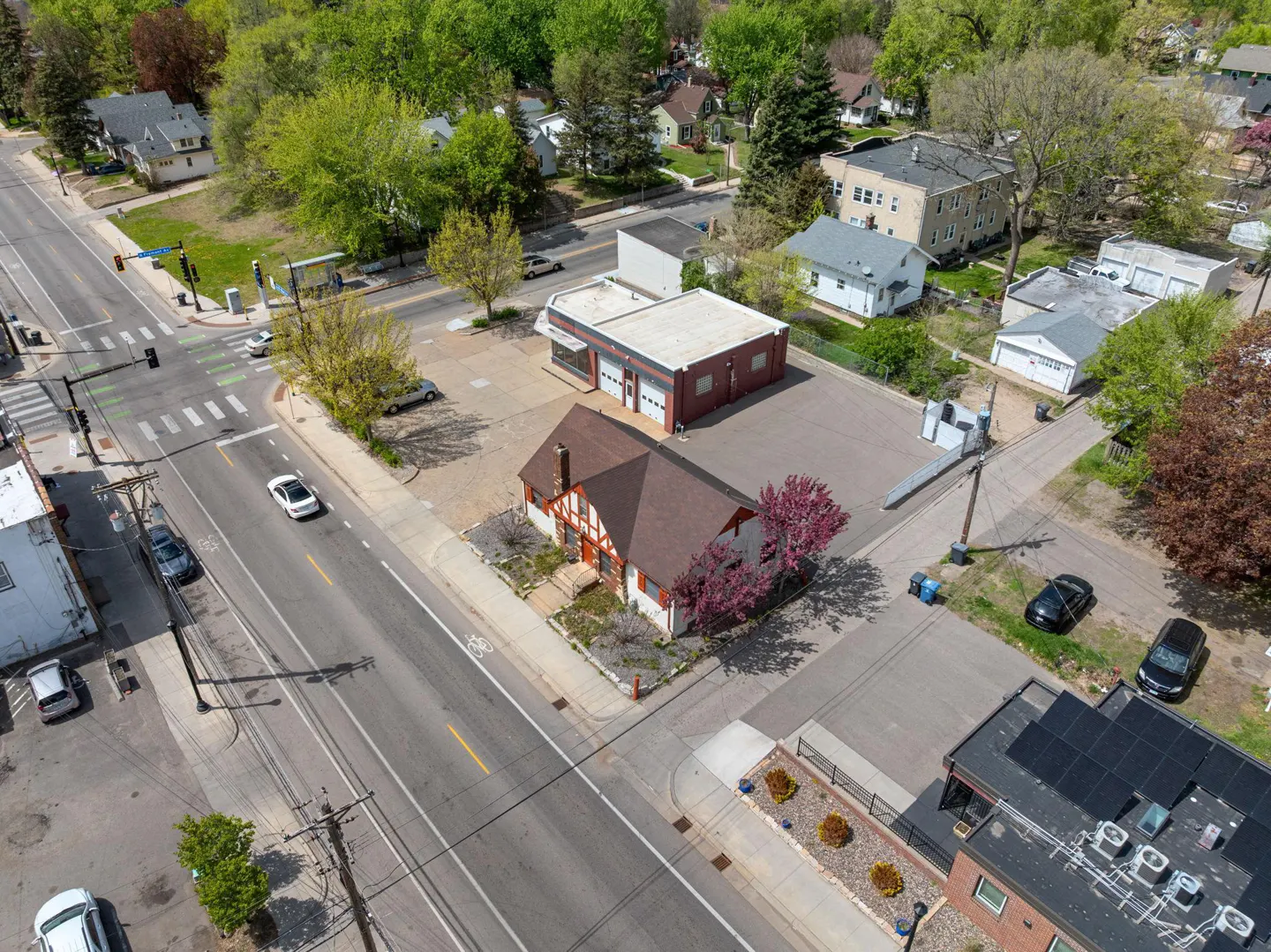 Aerial view of a neighborhood with a Tudor-style house, a red brick building, and cars on the street.