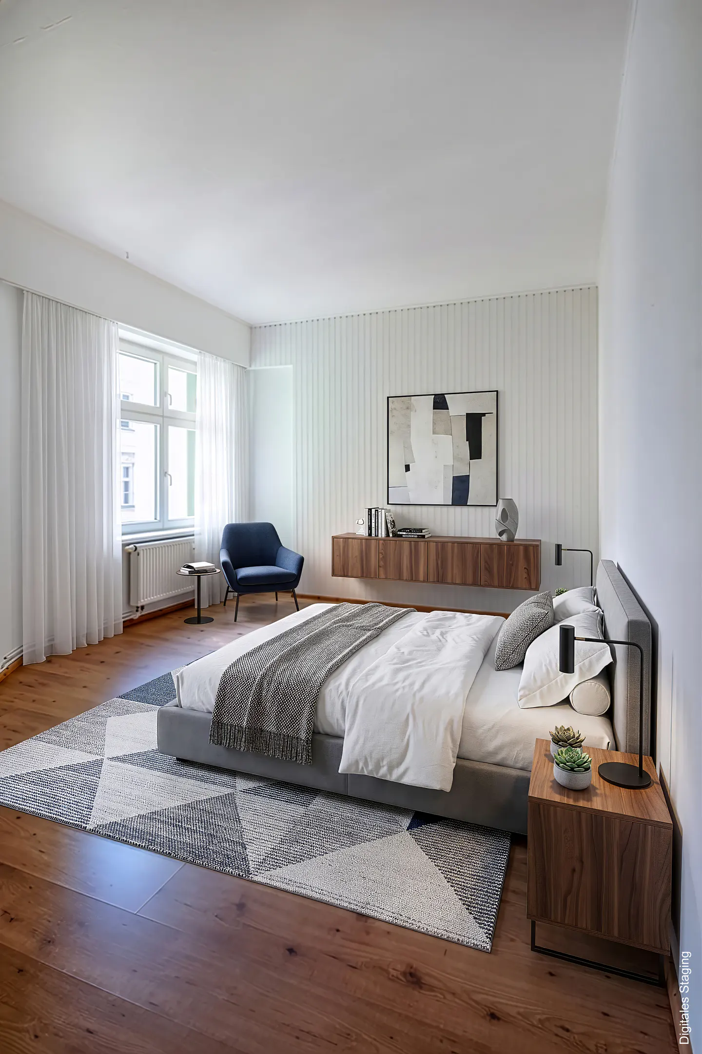 Bright bedroom with a gray bed, white linens, wood floors, and a geometric rug. A blue loveseat sits near a window with white curtains.