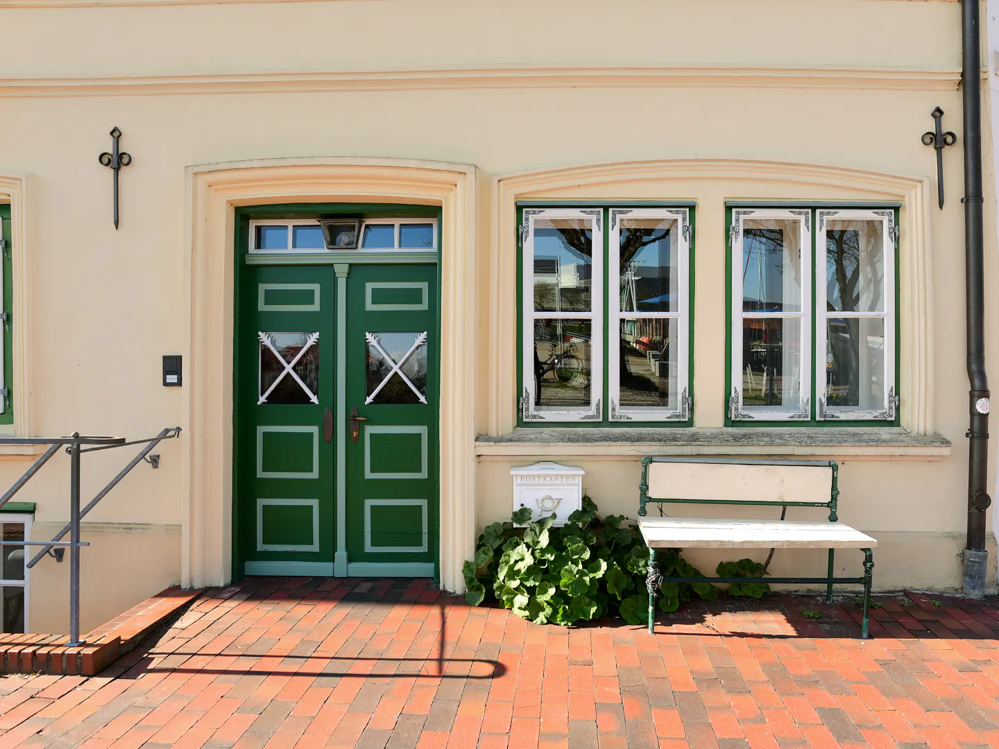 Facade of a building with a green door, white windows, and a bench on a brick walkway.