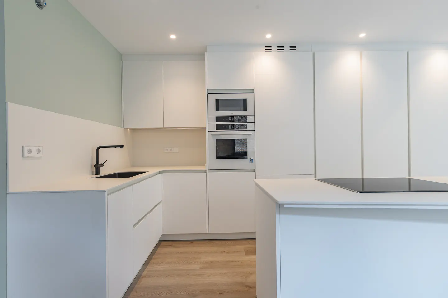 A modern kitchen with white cabinets, countertops, and appliances, including a black sink and stovetop.