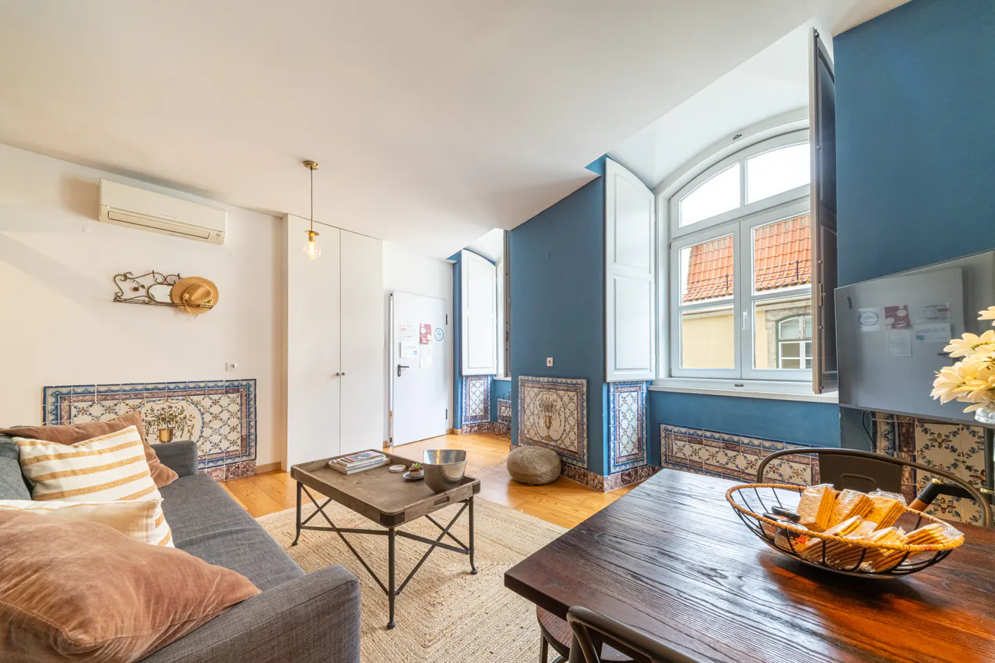 Bright living room with blue accent wall, white trim, and tiled accents. A gray sofa and wooden table sit on a woven rug.