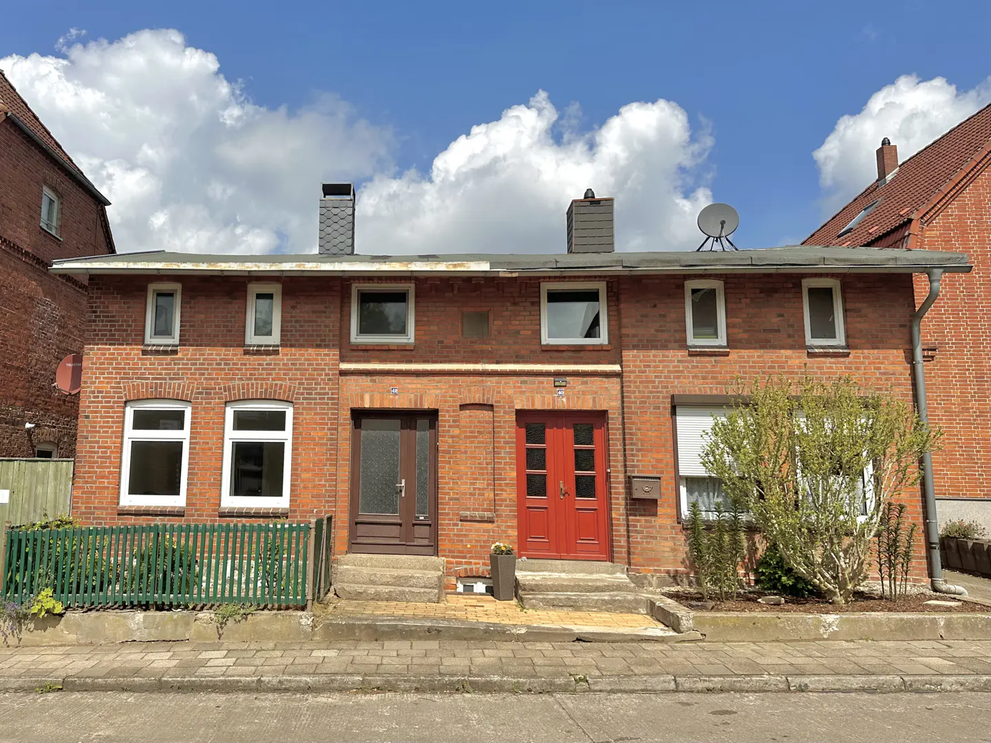 A two-story brick row house with a brown door on the left and a red door on the right.
