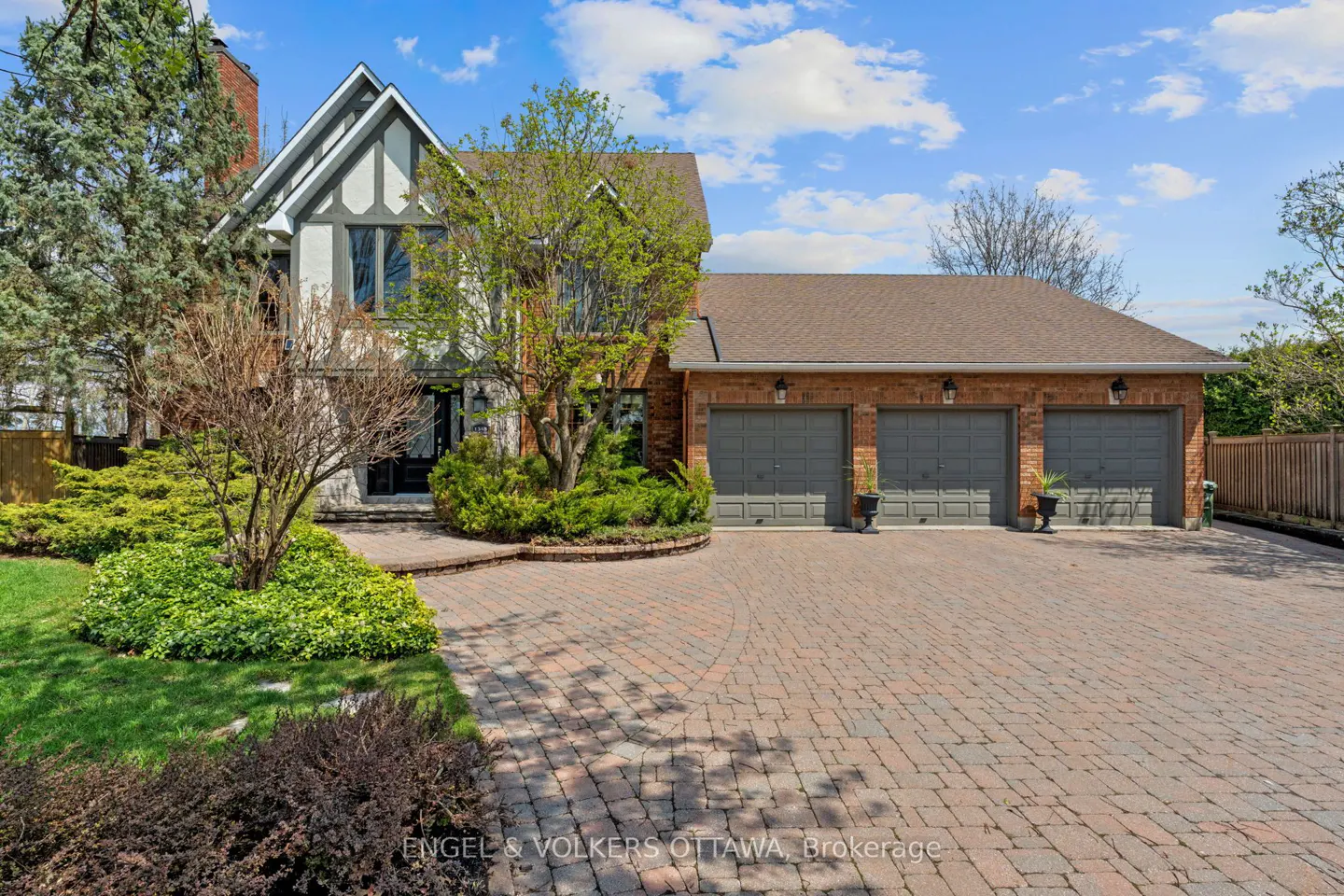 Exterior of a two-story house with a three-car garage and a brick driveway. The house has a Tudor-style facade and a well-manicured lawn.