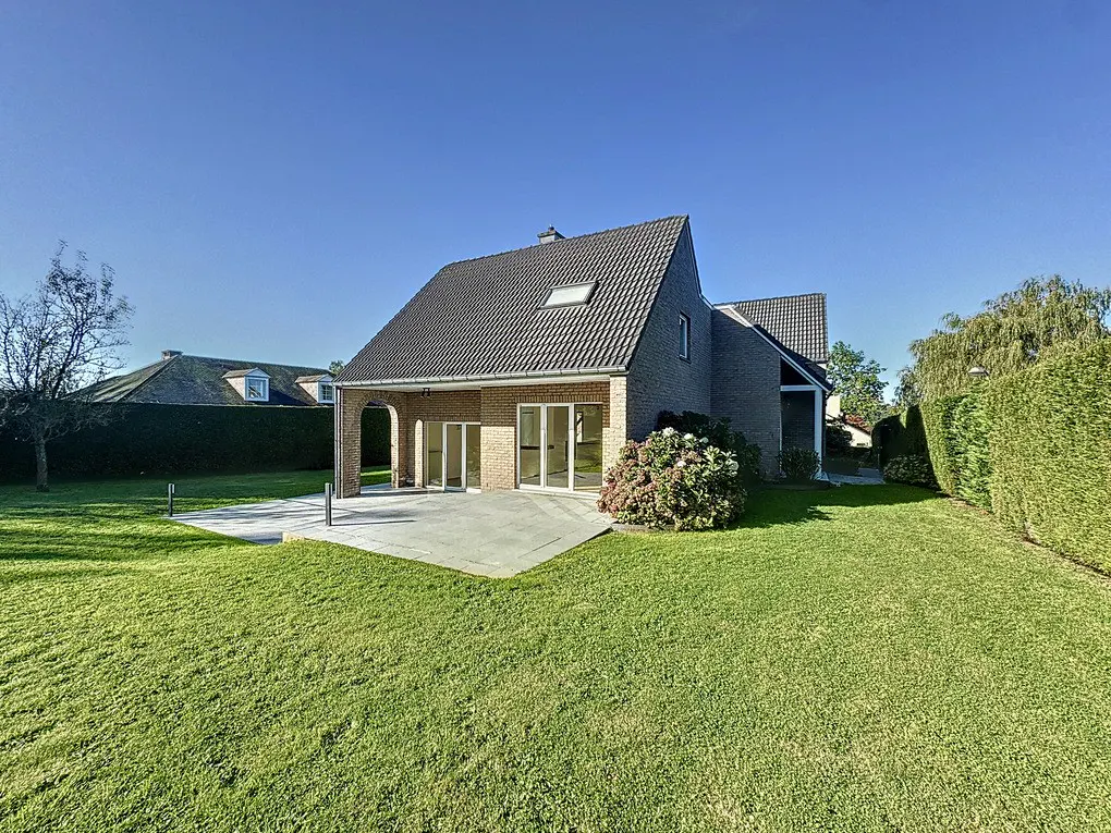 Exterior view of a gray brick house with a dark gray roof, a concrete patio, and a green lawn under a blue sky.