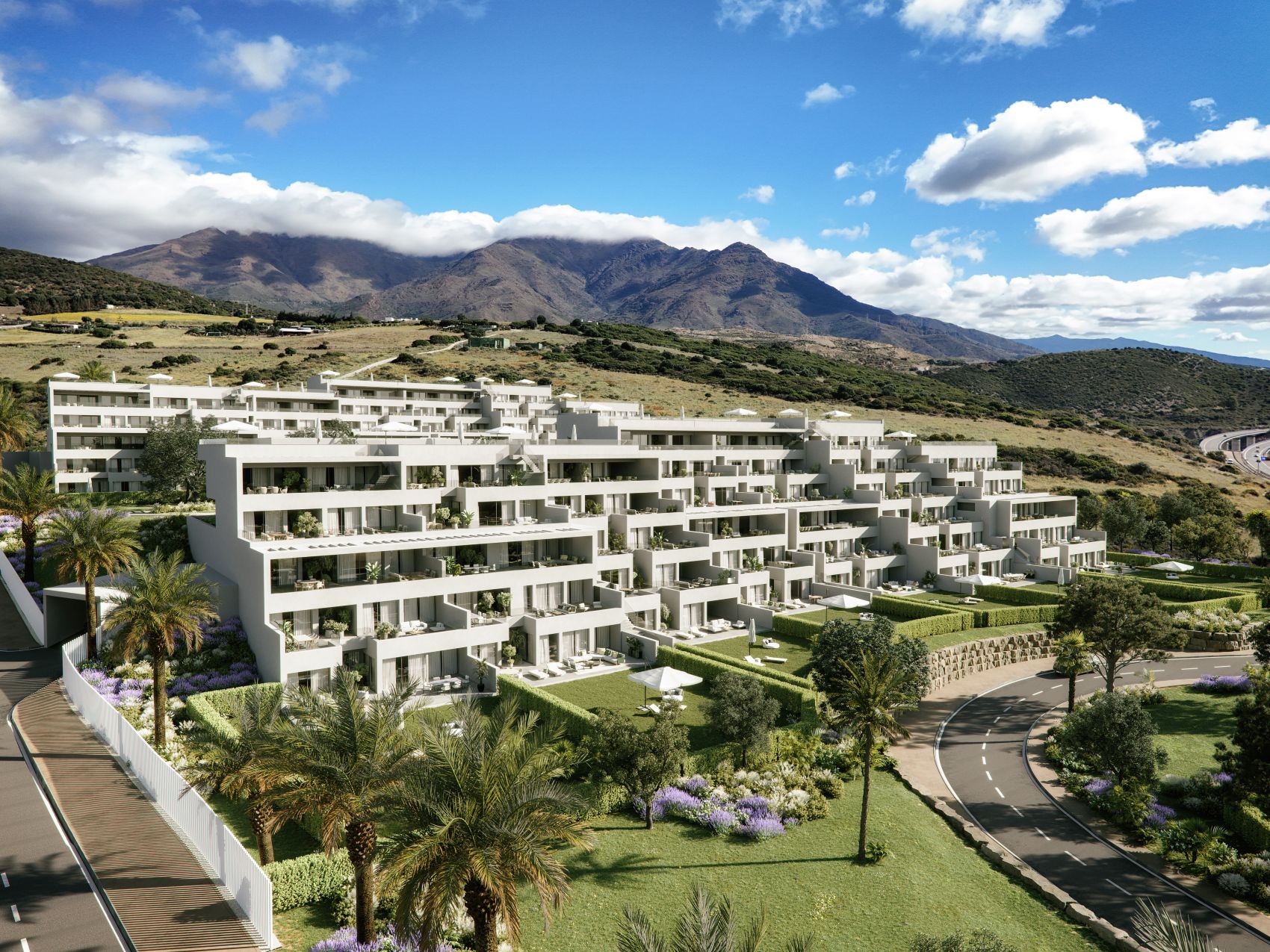 Modern white terraced apartment complex with balconies, surrounded by palm trees and green hills under a blue sky.