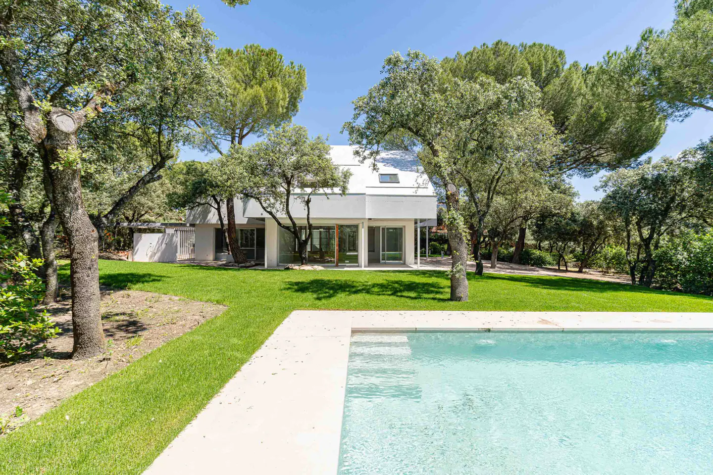 Modern white house with a pool, surrounded by green trees and lawn under a blue sky.