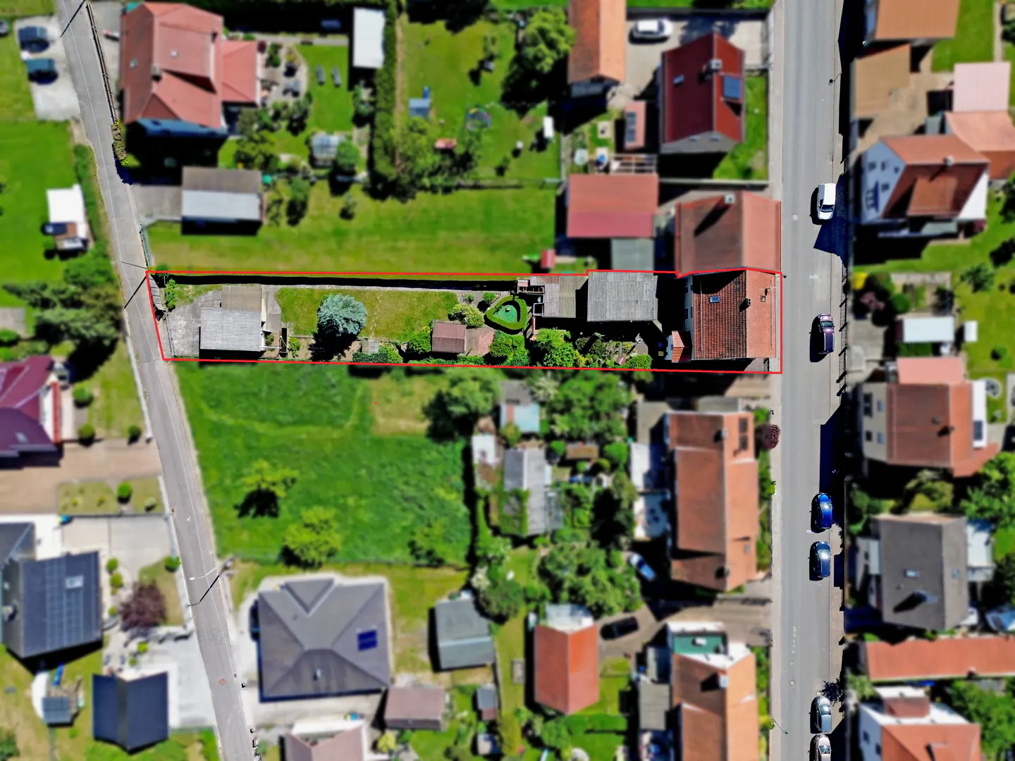 Aerial view of a long, narrow residential property outlined in red, featuring a house, garden, and outbuildings.