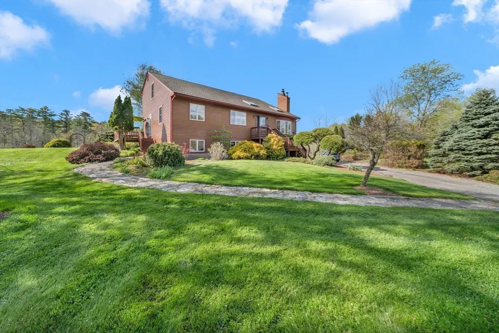 Two-story brown house with a green lawn, stone walkway, and blue sky with white clouds.