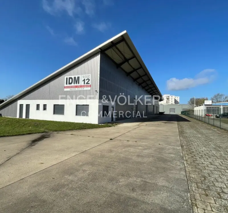 Exterior view of a large, modern, gray and white commercial building under a blue sky. "Engel & Völkers Commercial" is displayed on the building.