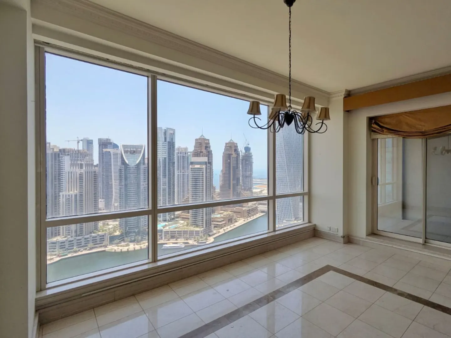 Bright room with marble floors, a chandelier, and floor-to-ceiling windows overlooking a Dubai marina skyline.