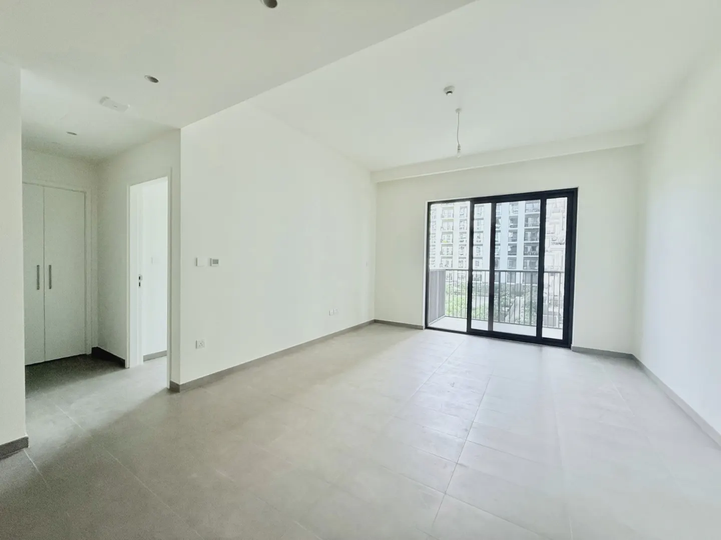 An empty room with white walls, gray tile floor, and a sliding glass door to a balcony.