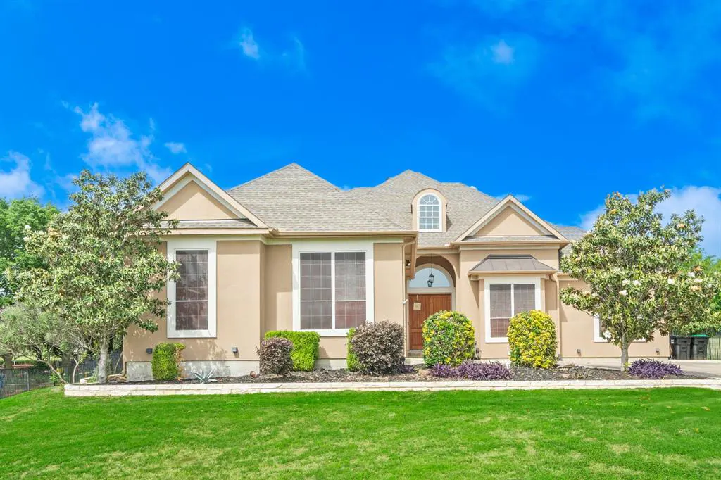 Beige single-story house with a gray roof, green lawn, and blue sky with clouds.