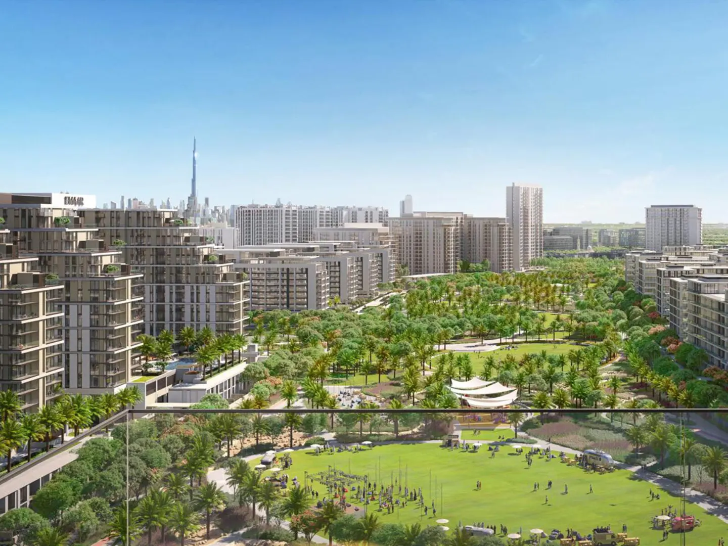 Aerial view of a modern city with beige buildings, green park, and the Burj Khalifa in the distance under a blue sky.