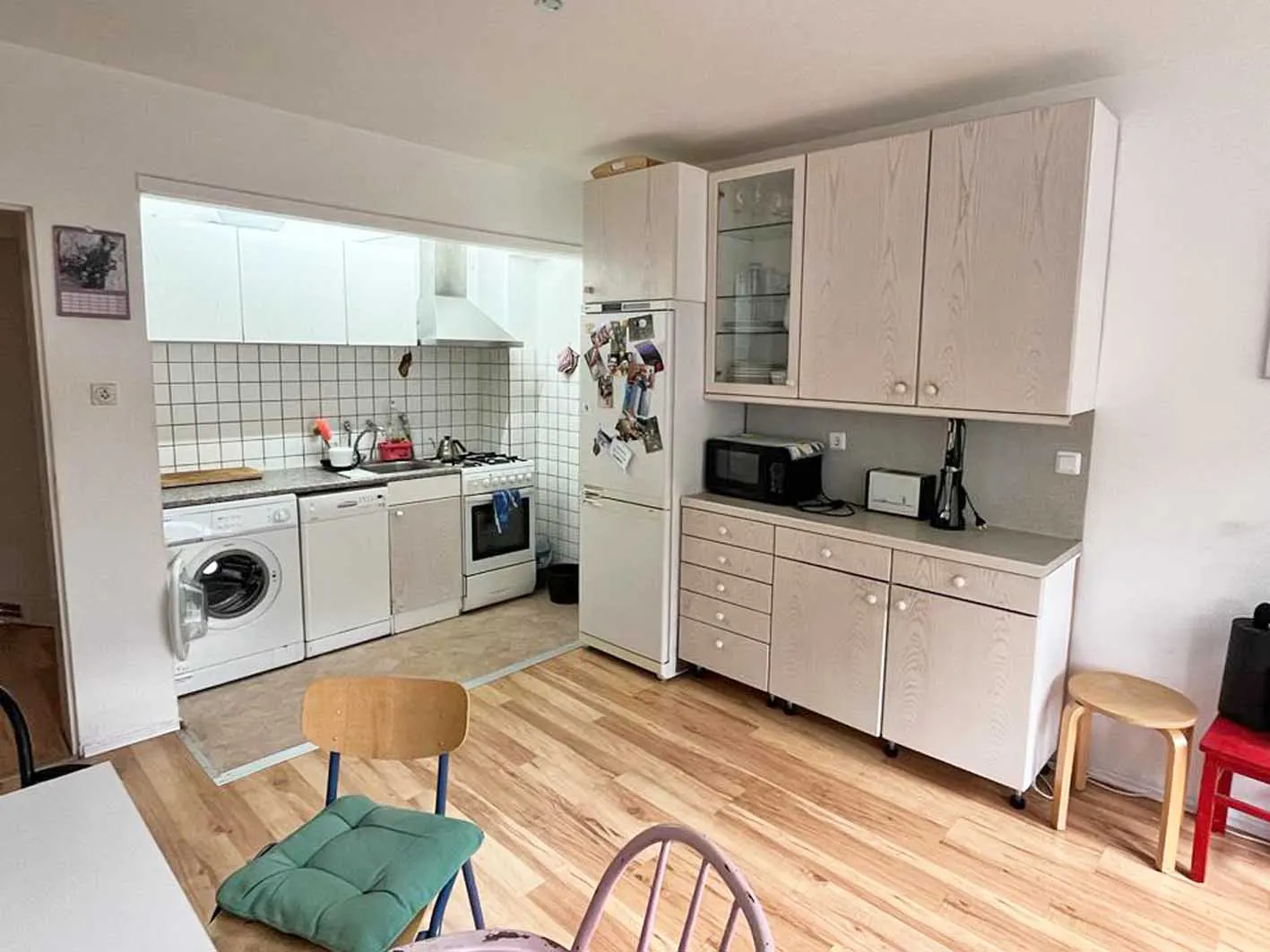 A bright kitchen with white appliances, cabinets, and a wood floor. A washing machine is next to a dishwasher and stove.