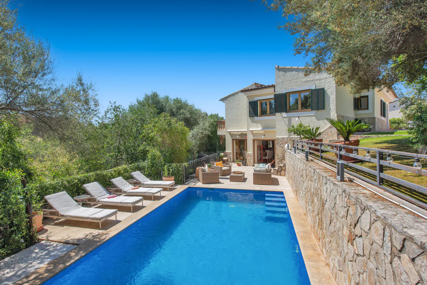 A sunny backyard with a pool, lounge chairs, and outdoor seating near a two-story house.