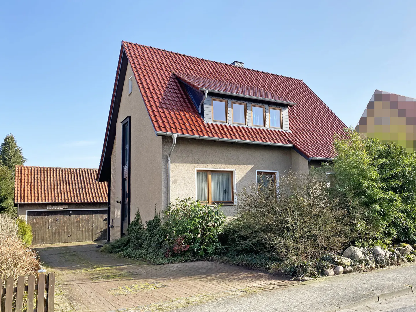 A beige two-story house with a red tile roof and a detached garage on a sunny day.