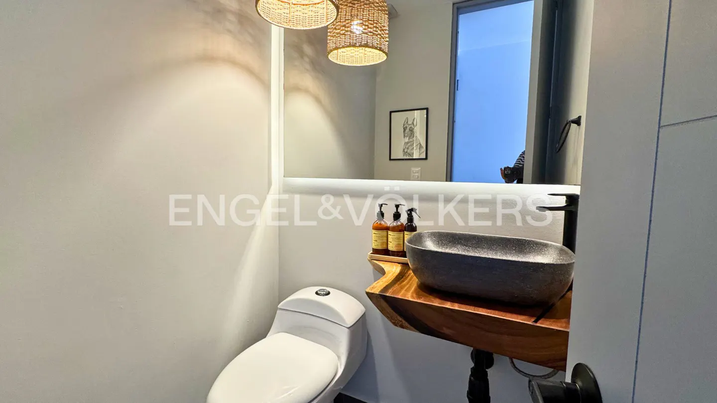 Bathroom with a white toilet, a stone sink on a wooden stand, and a mirror with lights above the sink.