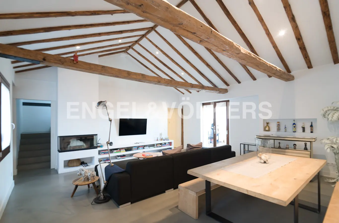 Bright living room with exposed wood beams, black sofa, fireplace, and light wood dining table.