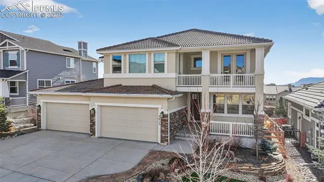 Two-story beige house with a two-car garage, stone accents, and a balcony under a blue sky.
