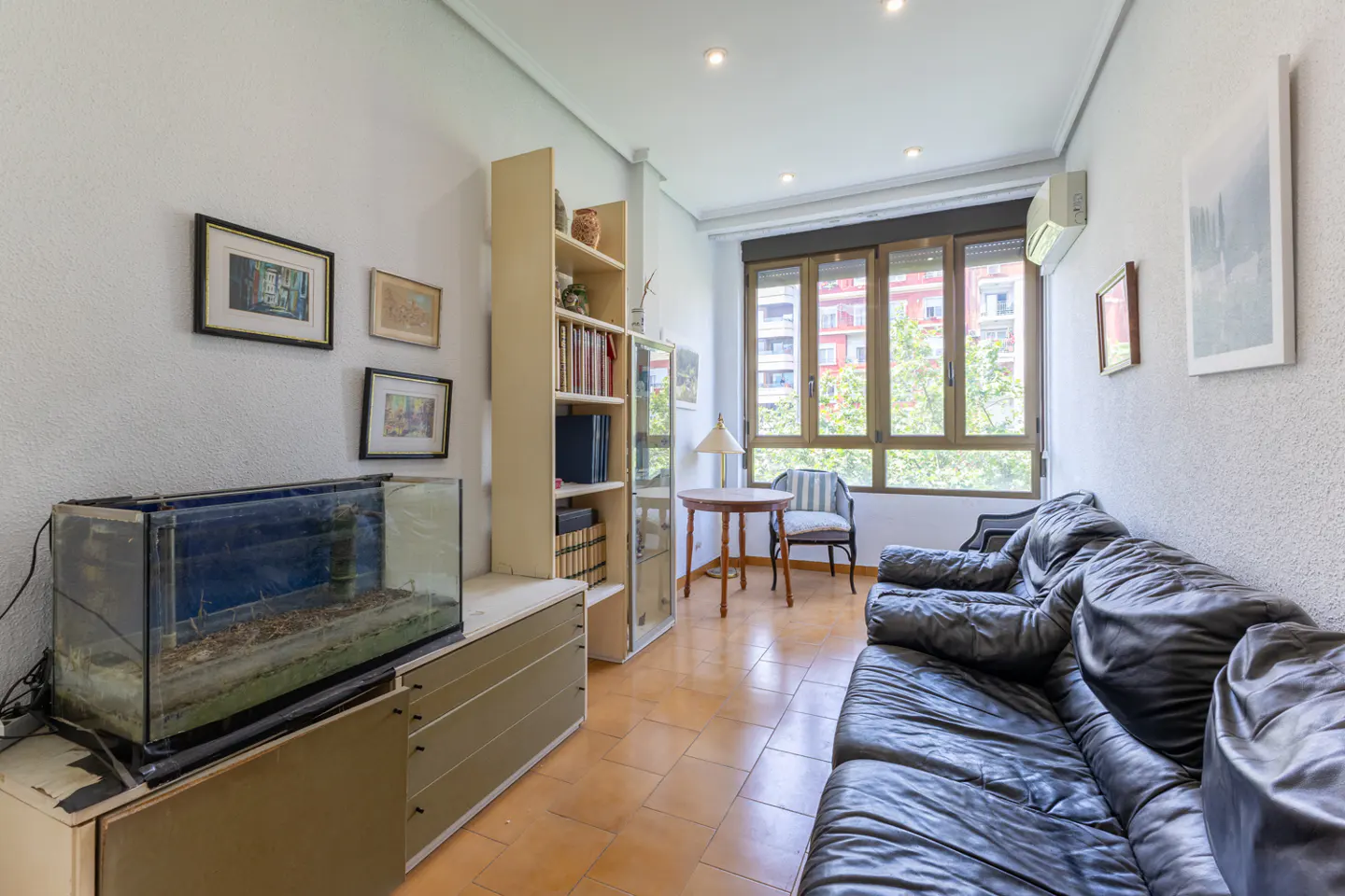A living room with a black leather sofa, a fish tank, and a window with a view of a building.