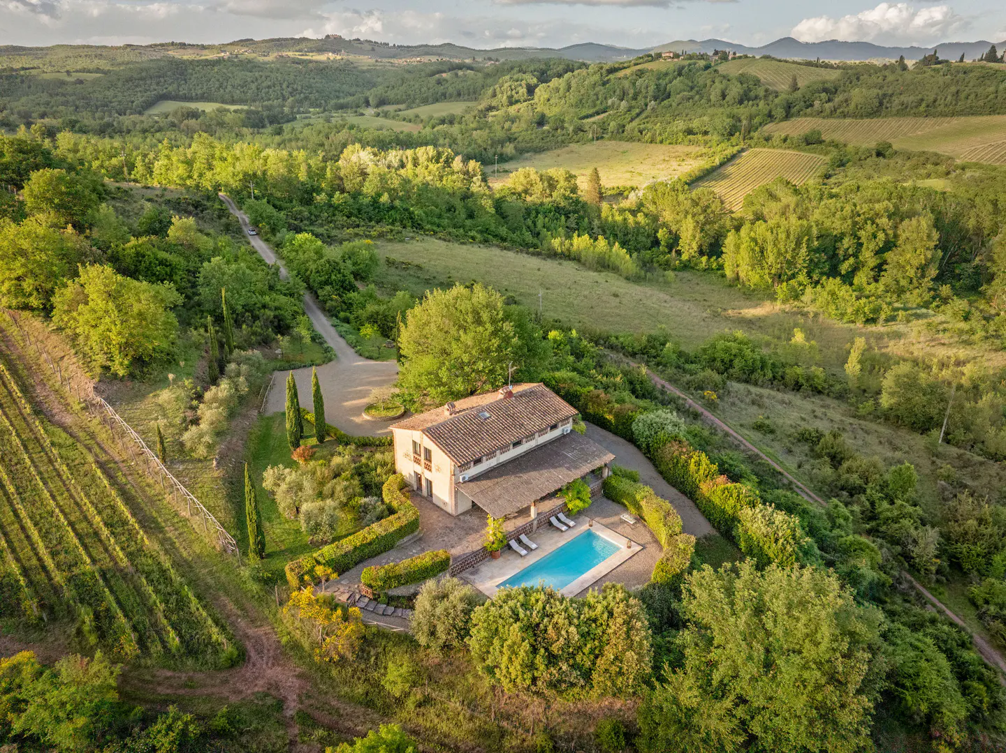 Aerial view of a Tuscan villa with a pool, surrounded by vineyards and green hills.