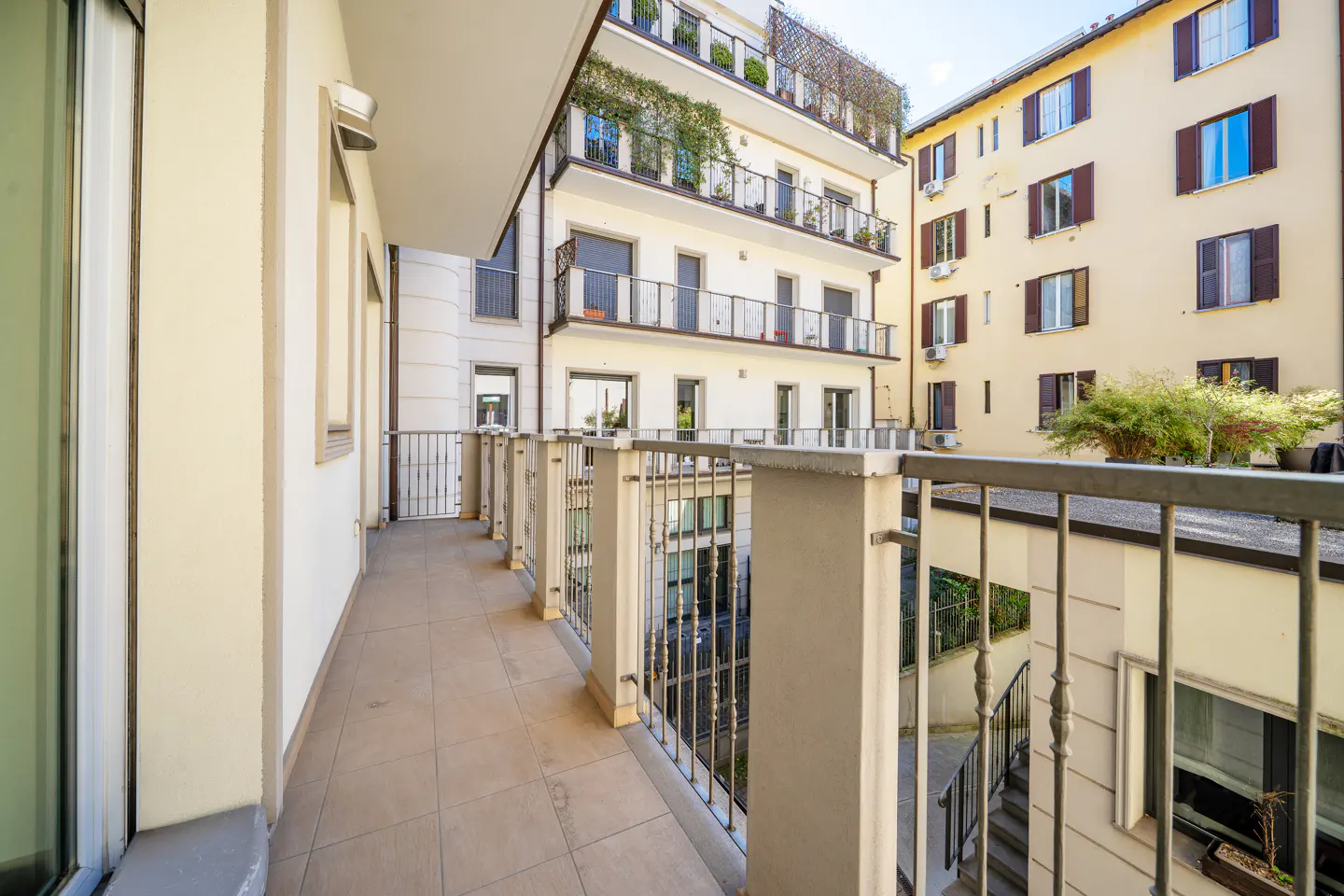 View from a balcony with a tile floor and metal railing, overlooking a courtyard with apartment buildings.