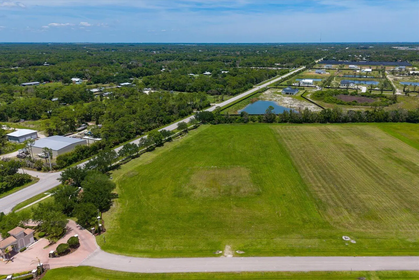 Aerial view of a large, green, vacant lot ready for development, with trees, roads, and houses in the background.