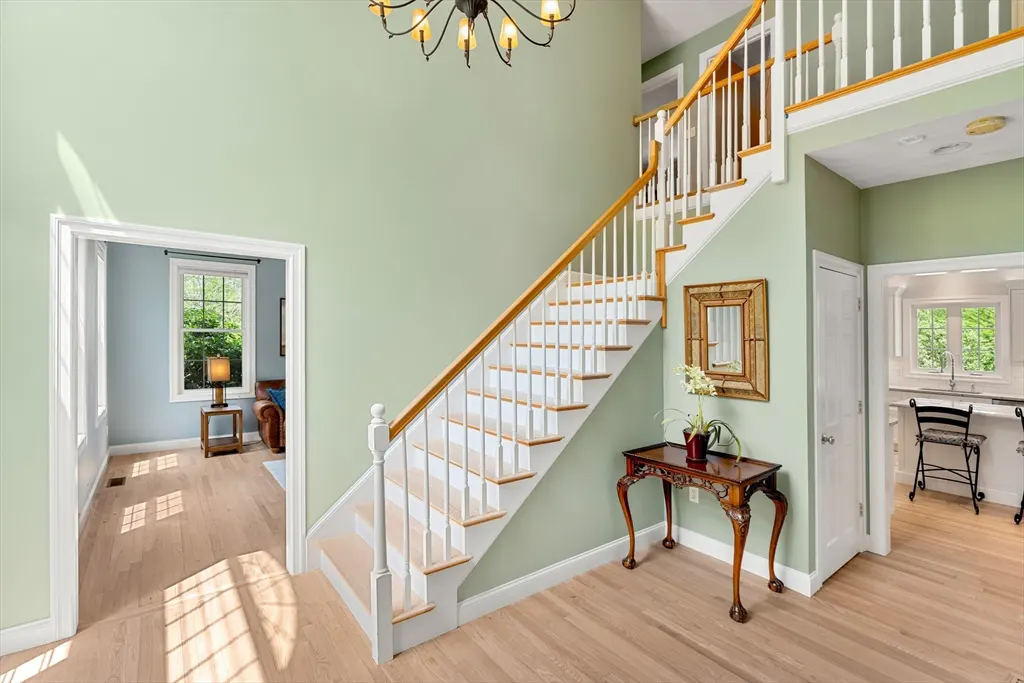 Light green foyer with a white staircase, wood floors, and a dark wood console table with a mirror above it.