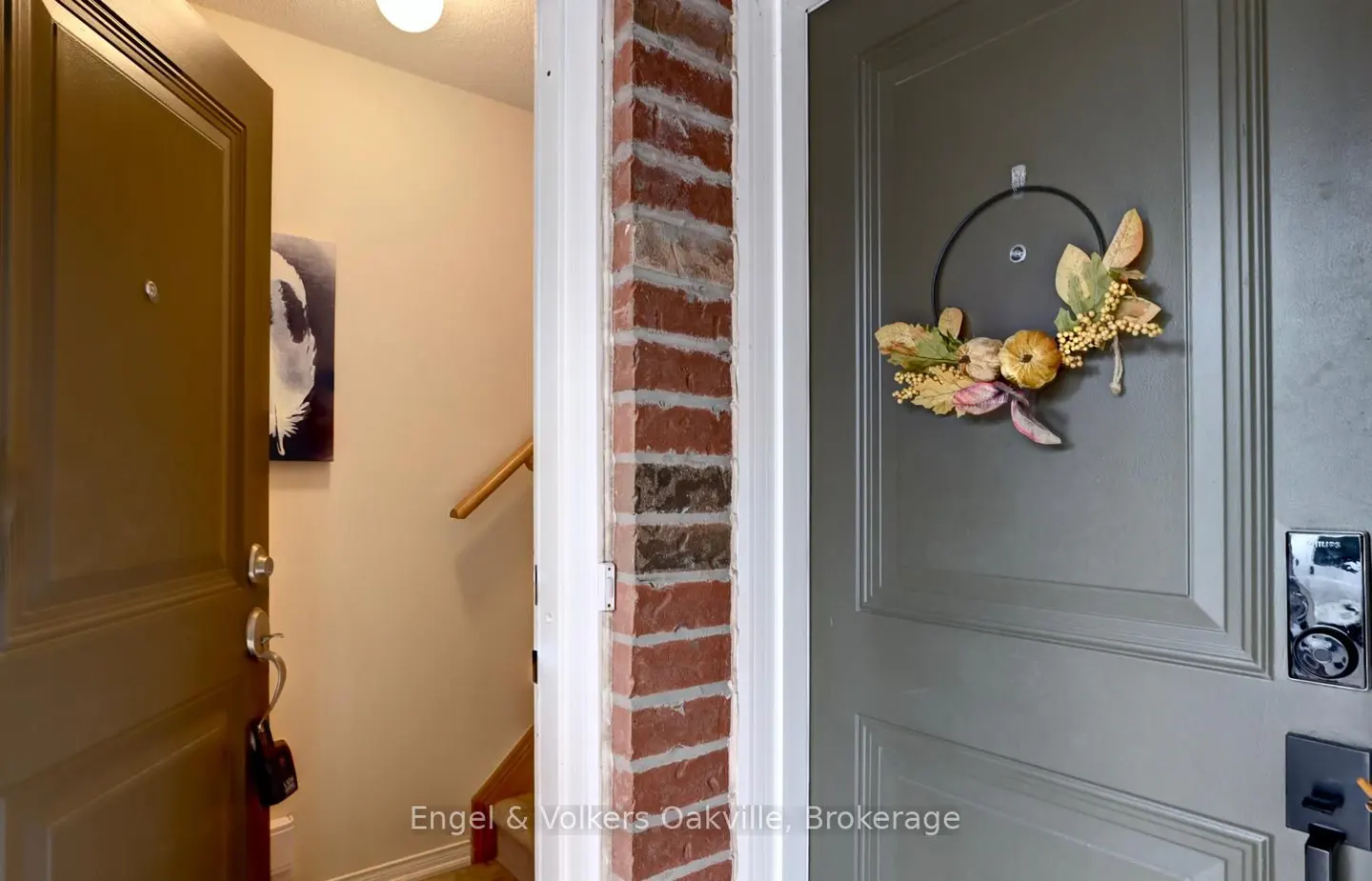 Open front door with a fall wreath on the gray door, and a brick column between the doors.