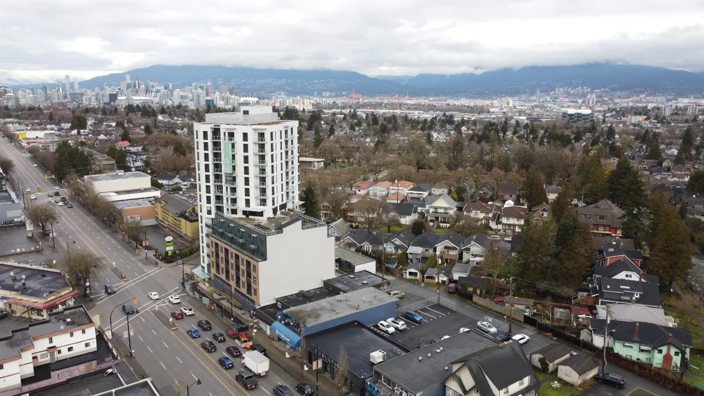 Aerial view of a modern white high-rise building in a city with mountains in the background.