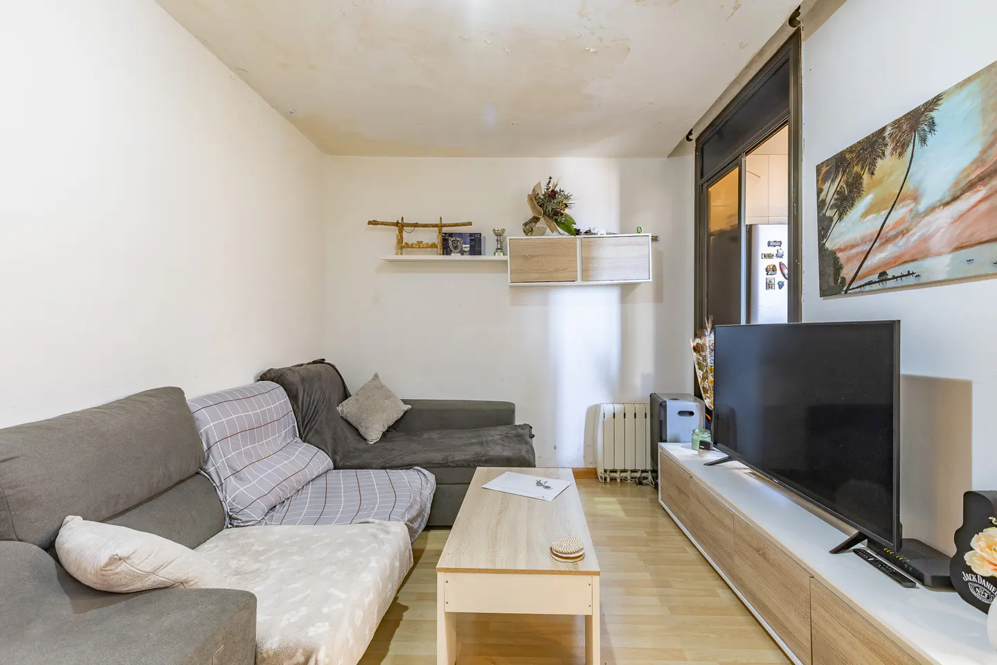 Living room with gray sofas, light wood floors, and a TV on a long console. Shelves and a painting decorate the white walls.