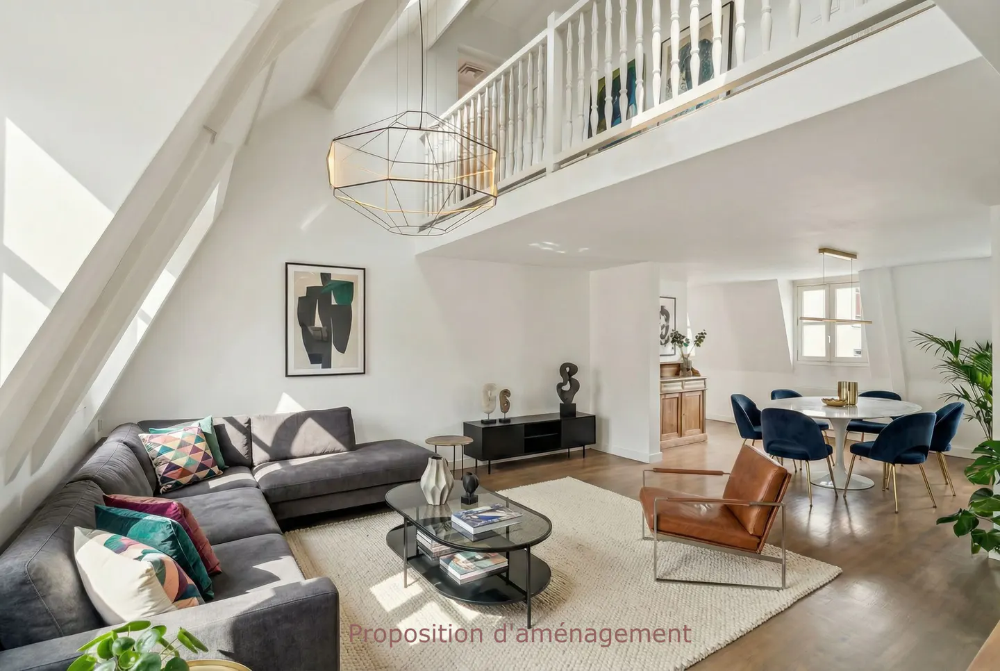 Bright, open living space with a gray sectional, brown leather chair, and a dining area with blue chairs. A white railing overlooks the scene.