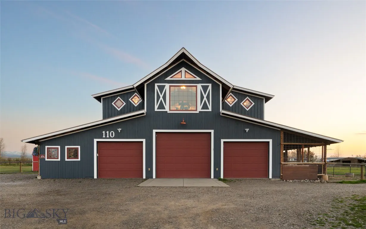 A gray barn with three red garage doors and white trim under a blue sky.