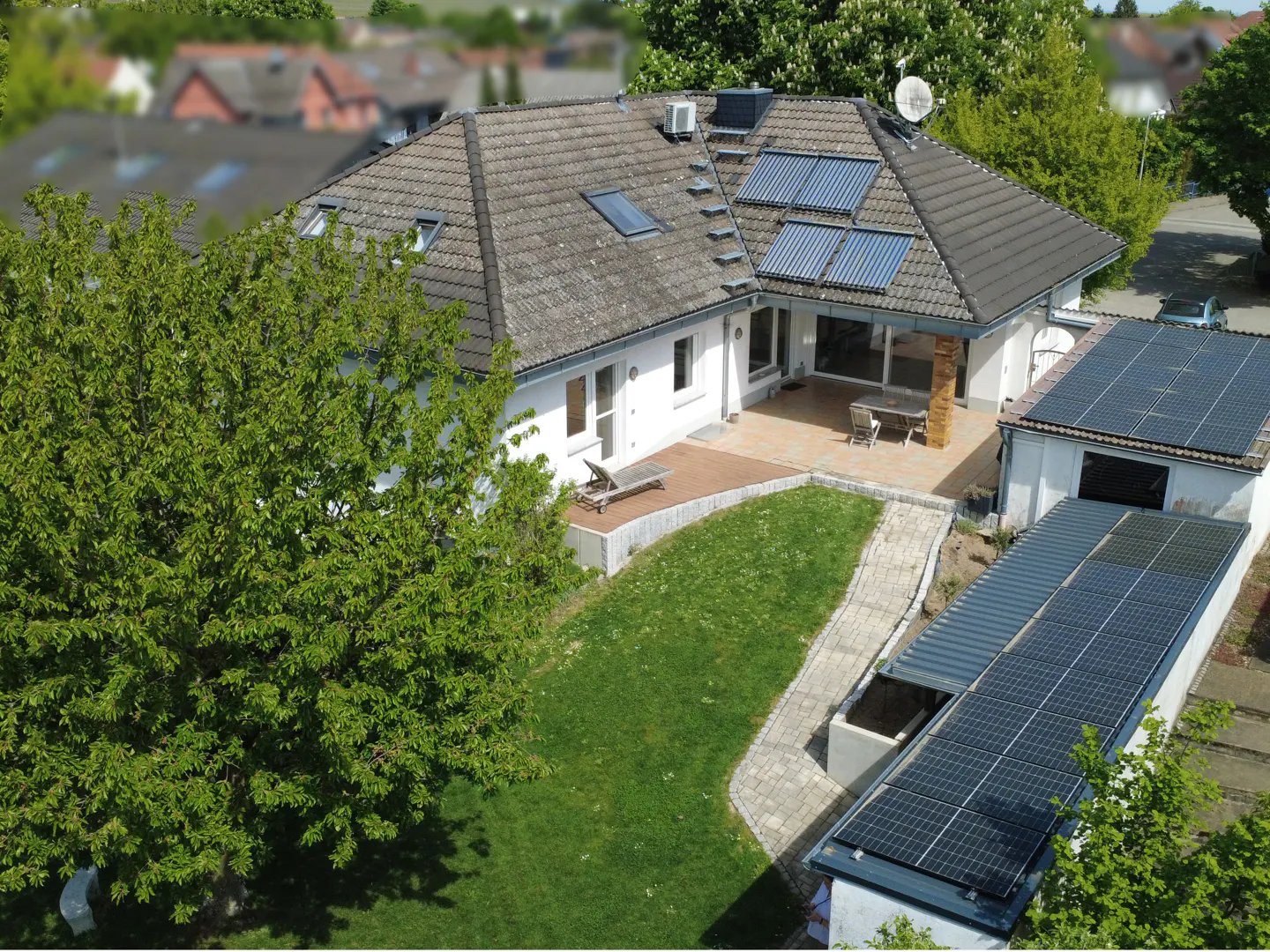 Aerial view of a white house with solar panels, a green lawn, and a patio with outdoor furniture.