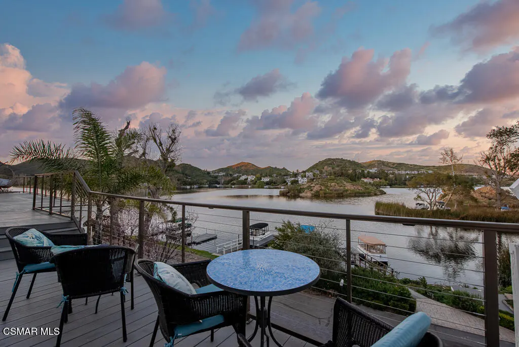 Outdoor patio with black wicker chairs and blue cushions overlooking a lake at sunset.