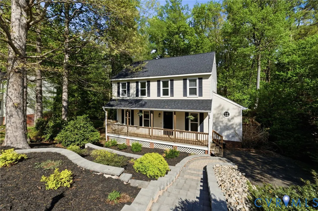 Two-story house with beige siding, black shutters, and a dark roof, surrounded by trees and landscaping.