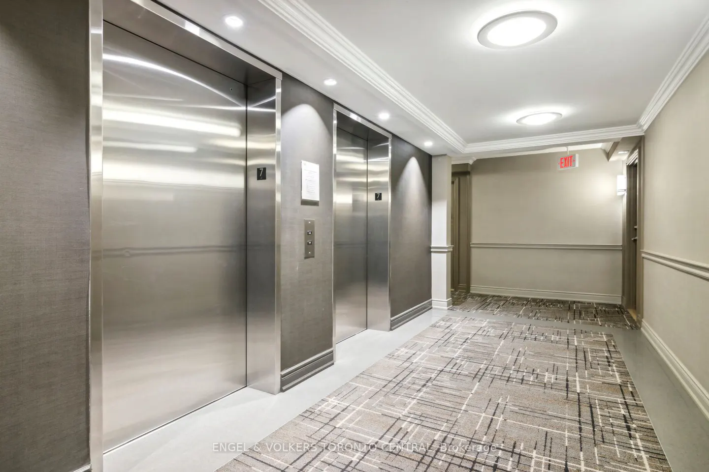 Hallway with three stainless steel elevators, beige walls, and a patterned gray carpet.