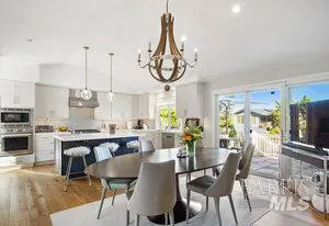 Open-concept kitchen and dining area with white cabinets, a dark blue island, and a wood chandelier over a dark wood table.