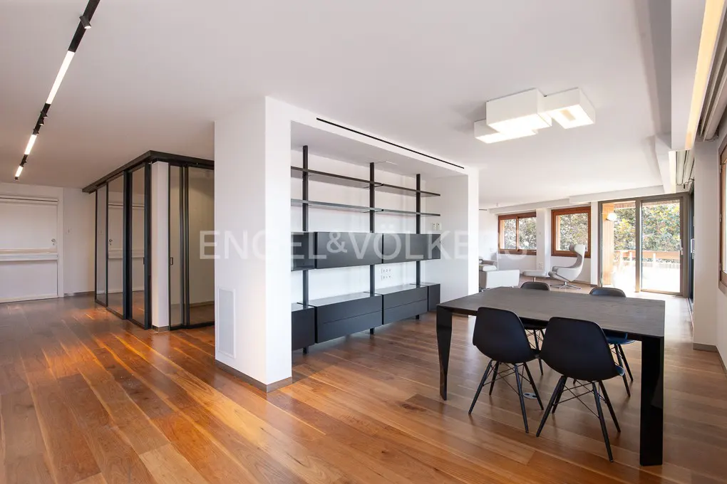 Bright, modern apartment interior with hardwood floors, black dining table and chairs, and a black shelving unit. Glass-enclosed room visible.