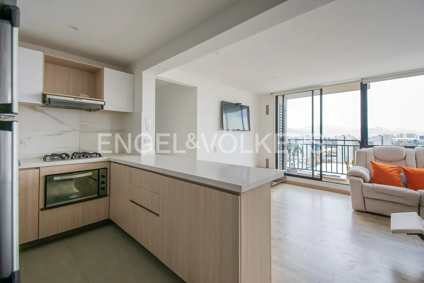 A bright, modern apartment interior with a kitchen, living area, and balcony overlooking a cityscape.
