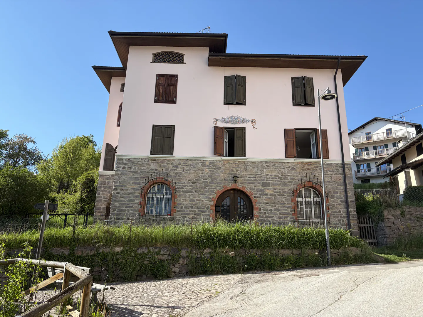 Two-story house with a stone base, pink stucco upper level, and brown shutters under a blue sky.
