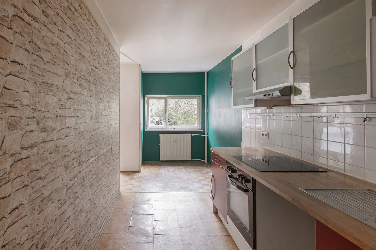 A kitchen with a stone wall, green wall, white cabinets, and a window.