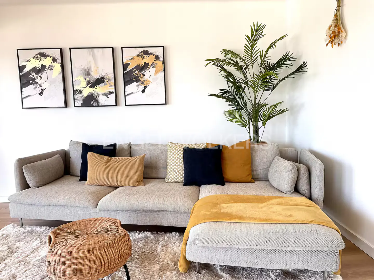 Living room with a beige sectional sofa, throw pillows, and abstract art on the wall. A wicker chair sits on a shag rug.